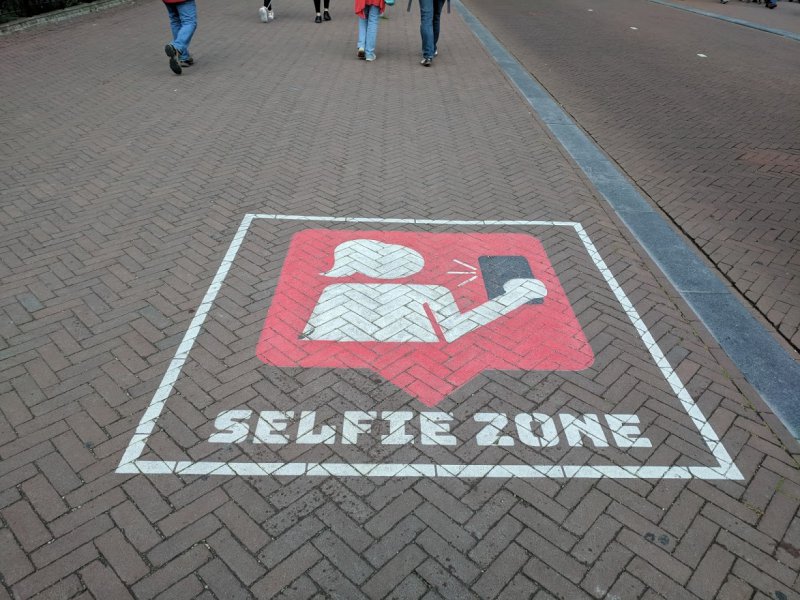 Sign painted on footpath with an image of a person taking a selfie, labelled "Selfie Zone"